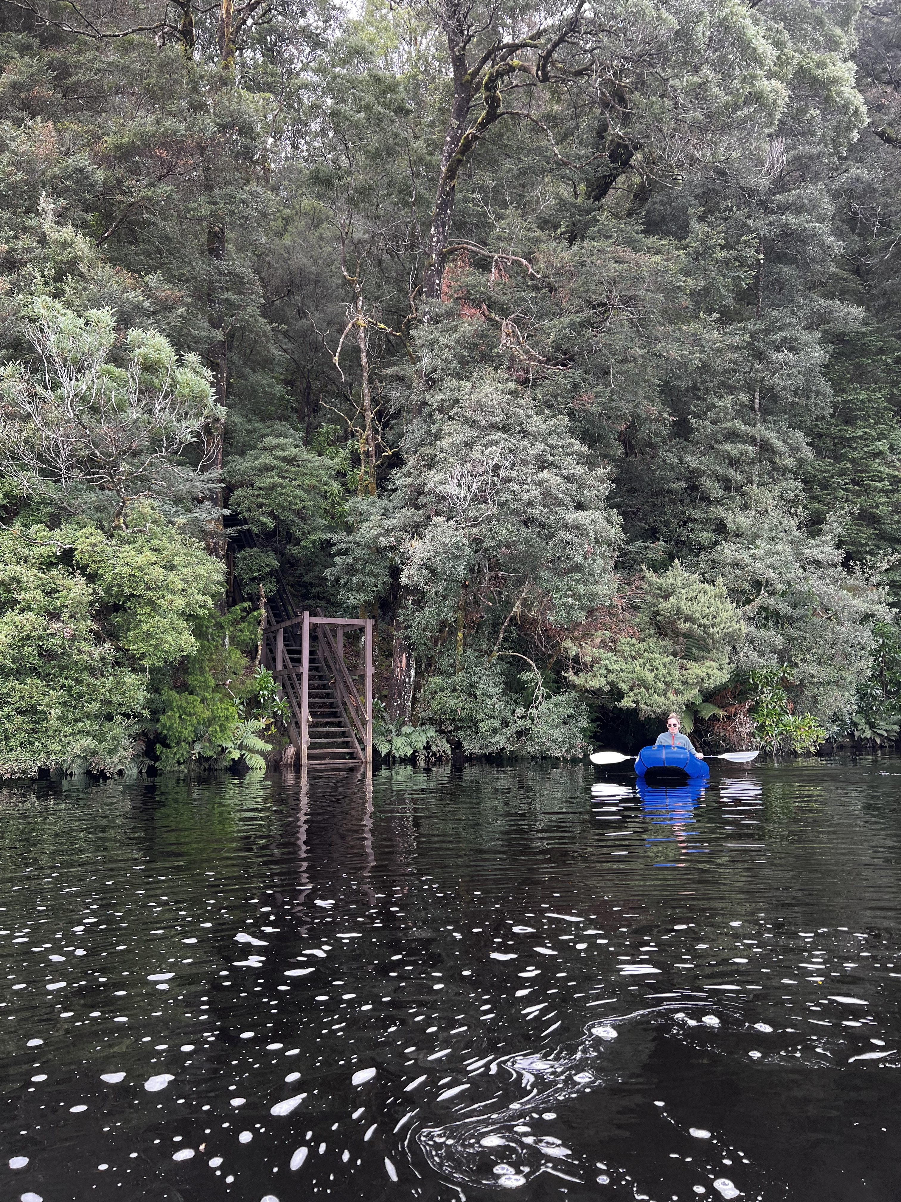 A person sits in a packraft with trees behind her