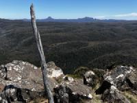 A stick in a pile of rocks with blue sky and mountains behind it