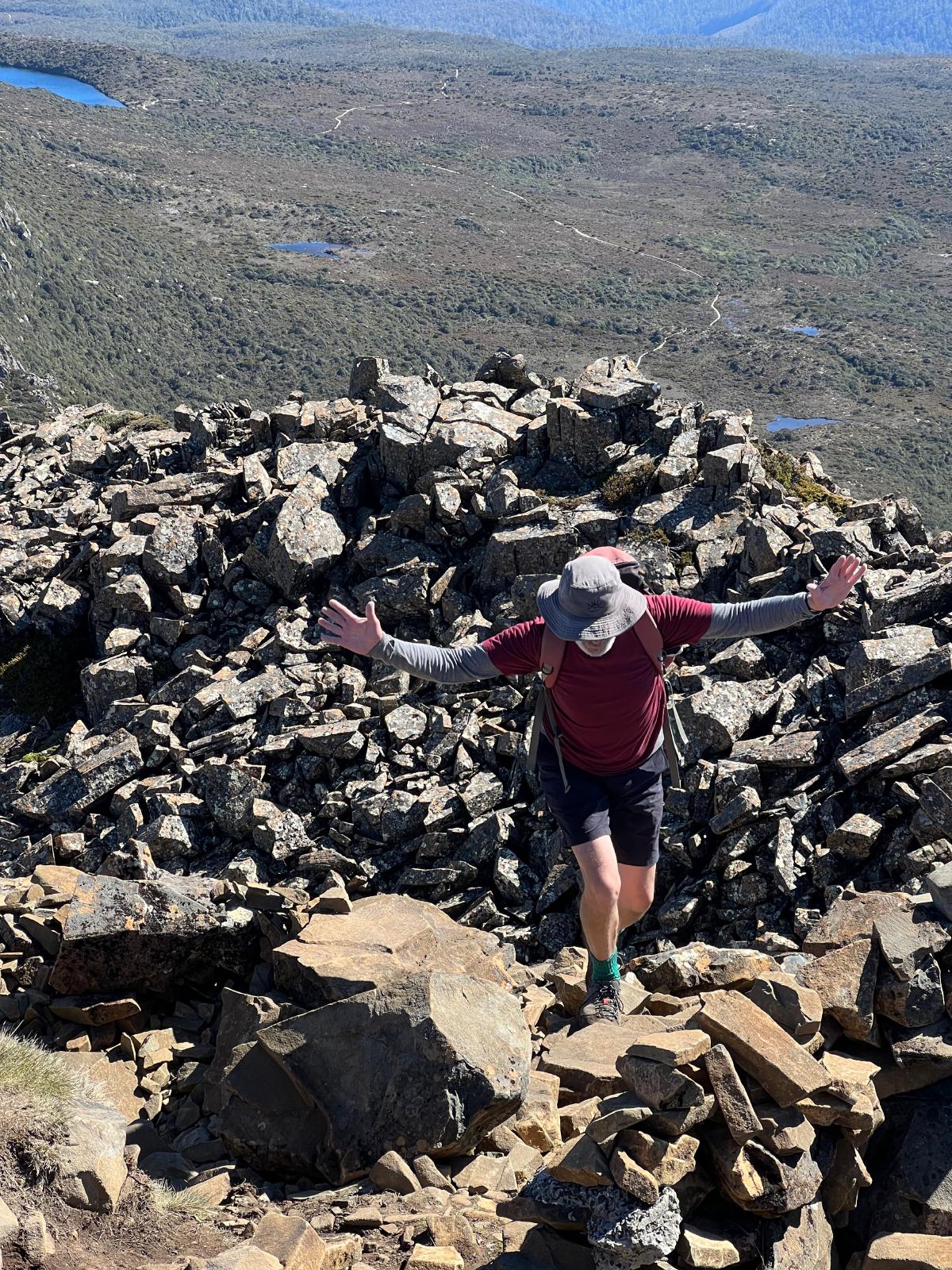A man nearly at the top of the mountain with his hands out