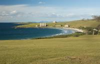 An open paddock flowing down onto a beach with old silos next to it