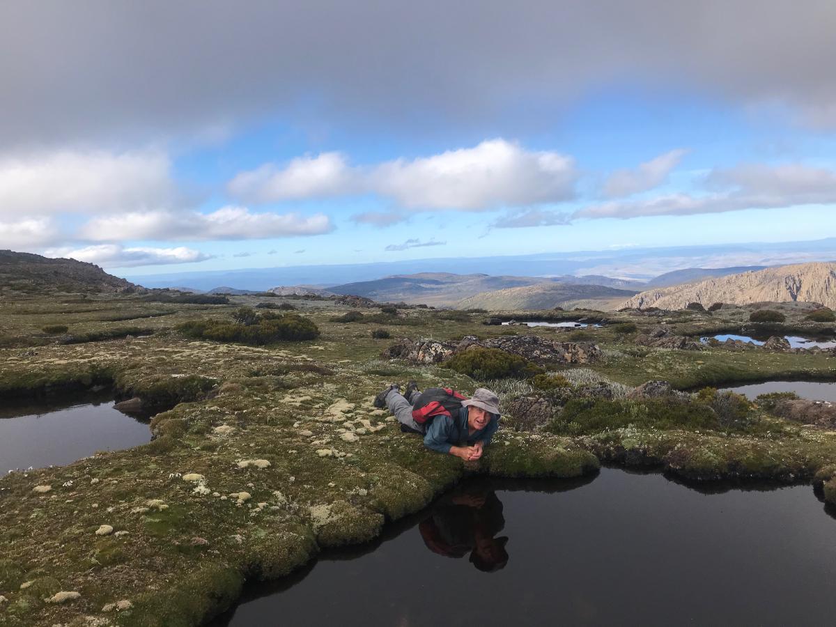 A man lying on the ground, about to take a drink from a waterhole