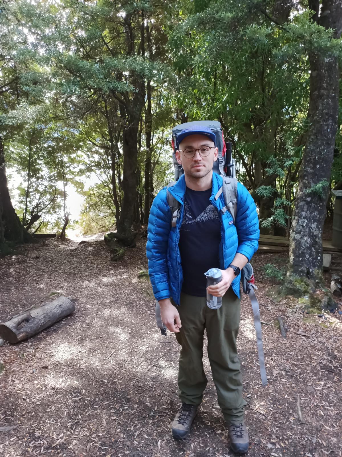 A man standing in a clearing in the bush looking at the camera