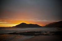 A sunsut picture with mountains in the background and the ocean in the foreground